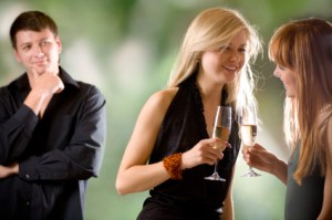 Two women holding glasses with champagne and laughing, young man looking at them and smiling, outdoors, focus on women